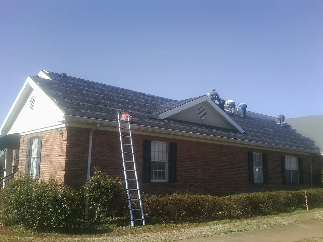 Crew tearing shingles off a brick ranch roof with a ladder set — Metal Roof Repair work by our crew in York Beach