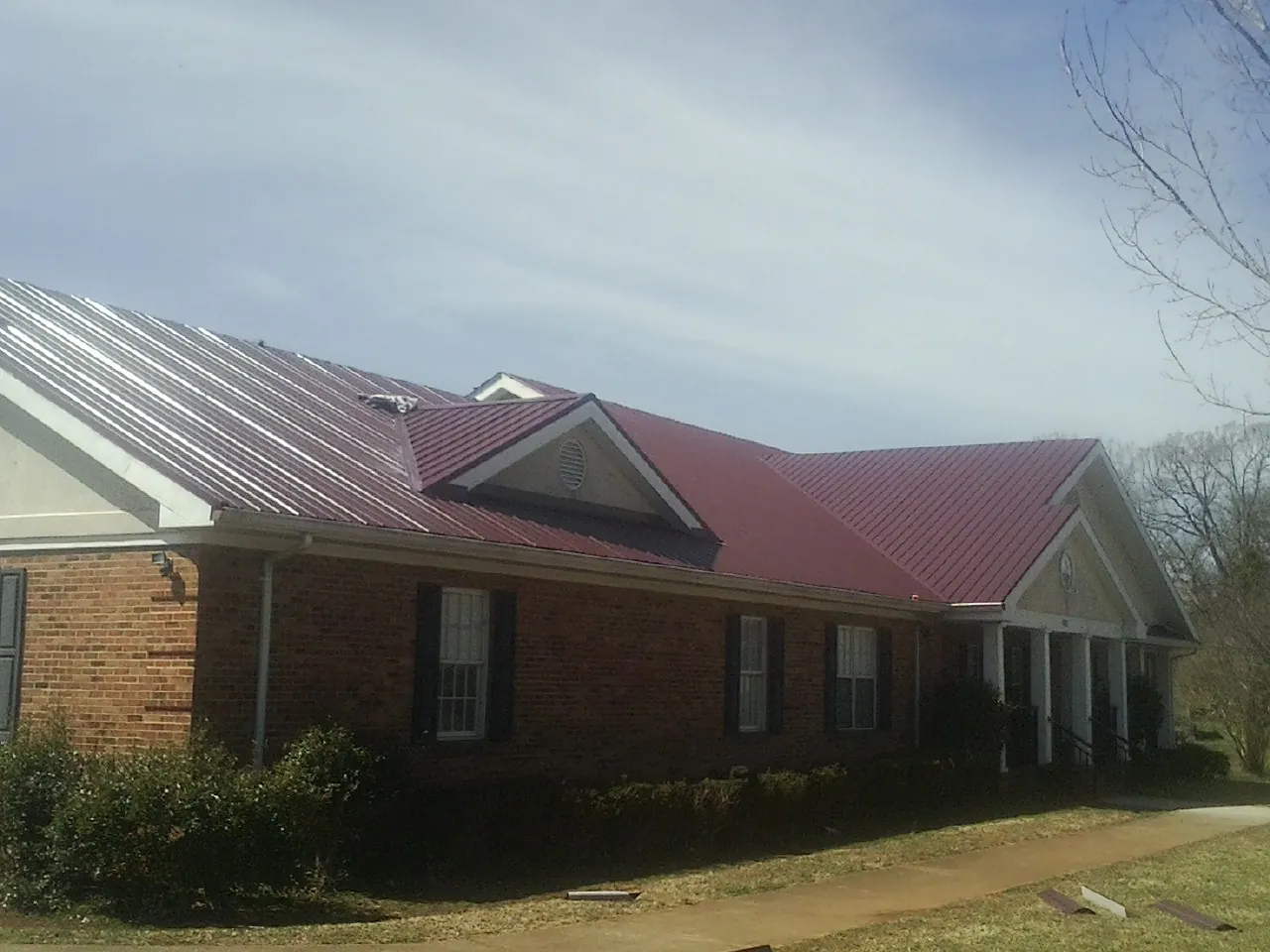 Red metal roof with gabled entries on a long brick building, from a Hail Damage Roof Repair job in York Beach