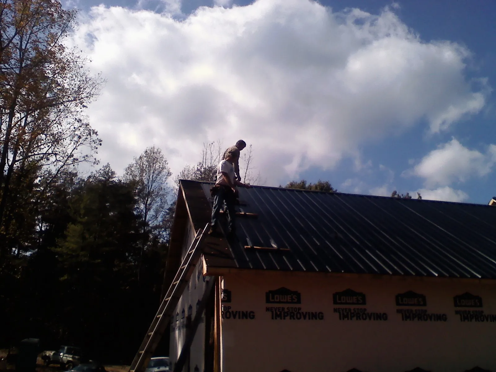 Roofer fastening dark metal panels high against a cloudy sky, from a Roof Inspection job in York Beach