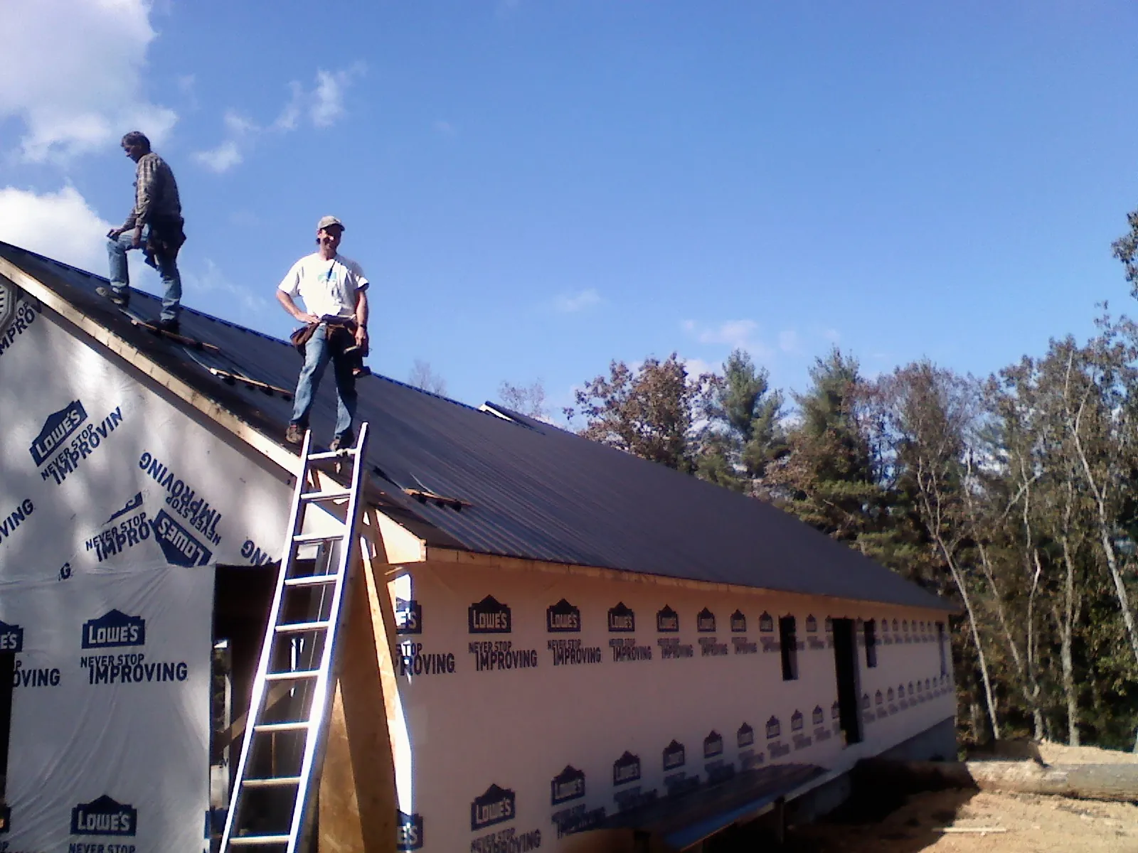 Two roofers standing on a long dark metal roof over a wrapped building in York Beach