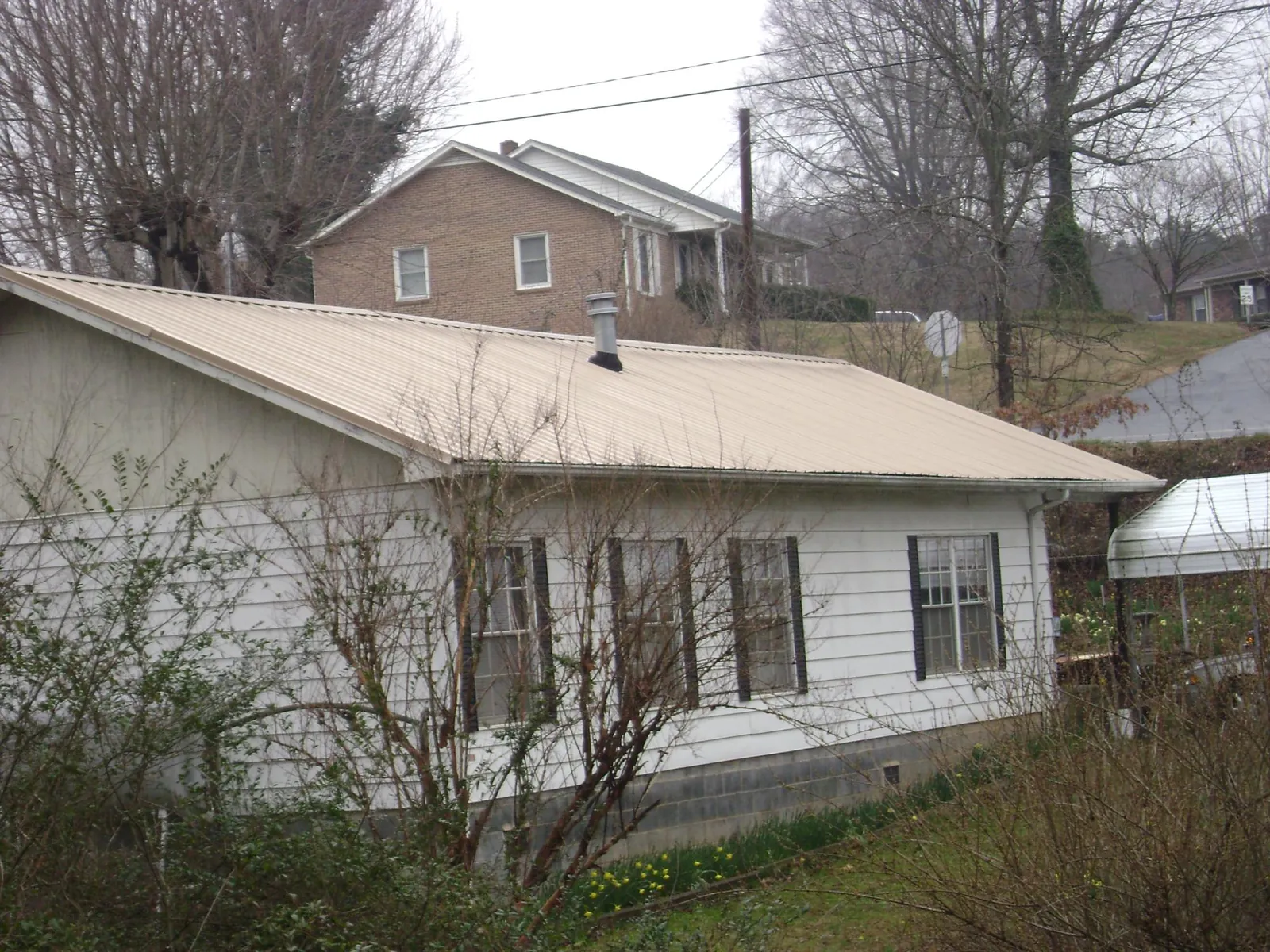 Tan metal roof on a white sided house set into a hillside — Commercial Roofing by Roofing Brothers in York Beach